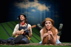 Two performers in farmer's costumes on stage, one playing a small guitar, one playing a small tin penny whistle