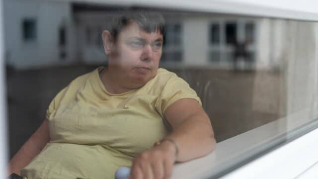 A woman in a wheelchair, looking out at the world through the window