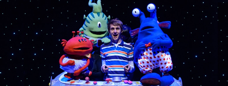 A performer surrounded by alien puppets