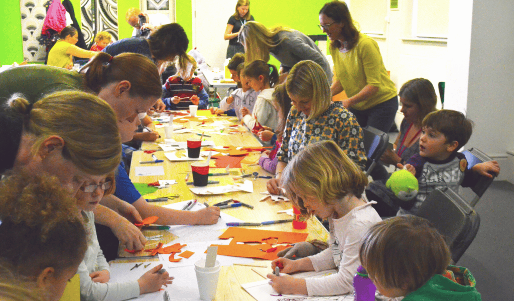 Children and adults gather around a long table, taking part in craft activities