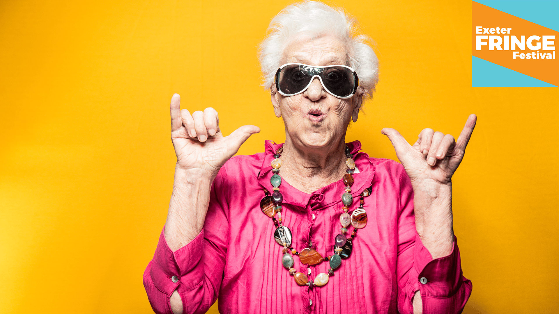 Promotional image for Cafe Theatre: An older woman with white hair in a vibrant pink shirt against an equally vibrant yellow background giving us the 
