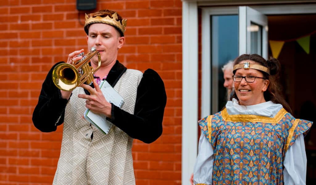 Newcourt Community Festival 2021 Two people wearing medieval clothes and crowns, one is blowing a trumpet