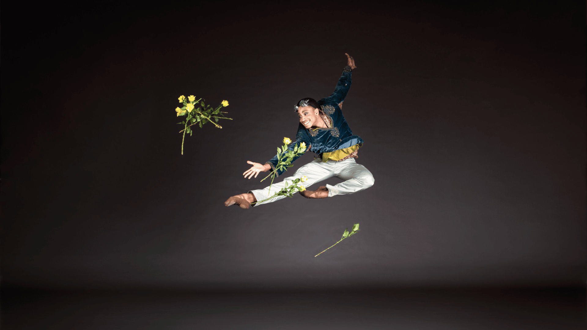 A ballet dancer leaps into the air, throwing flowers around them