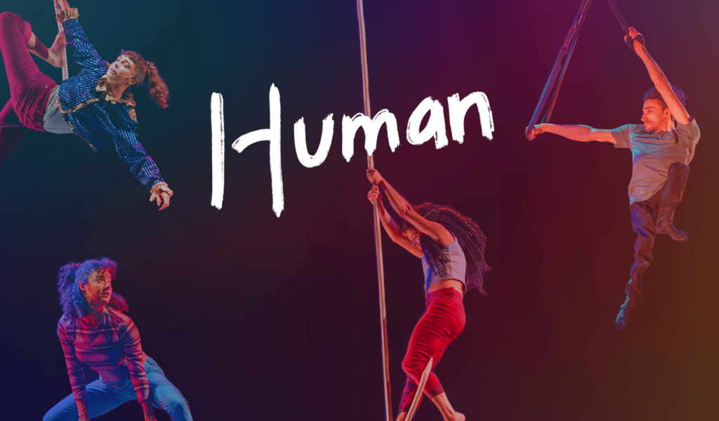 Human artwork - three performers hang in the air holding onto aerial ropes, another performer crouches on the ground looking up at them