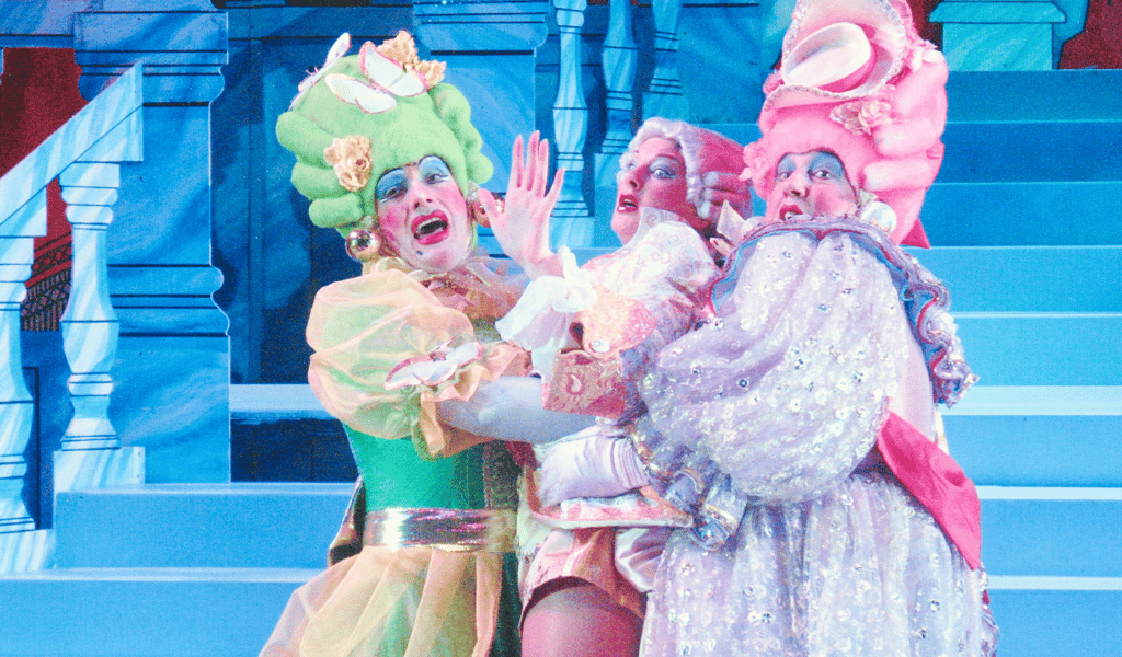 Three performers wearing colourful panto outfits look shocked