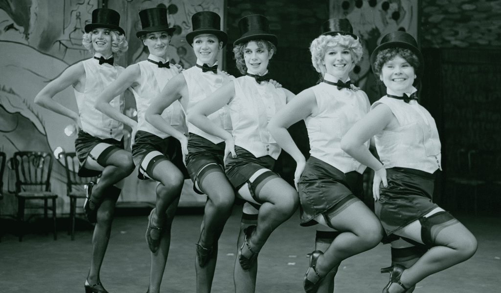 Six cabaret dancers raise their knees while standing in a line