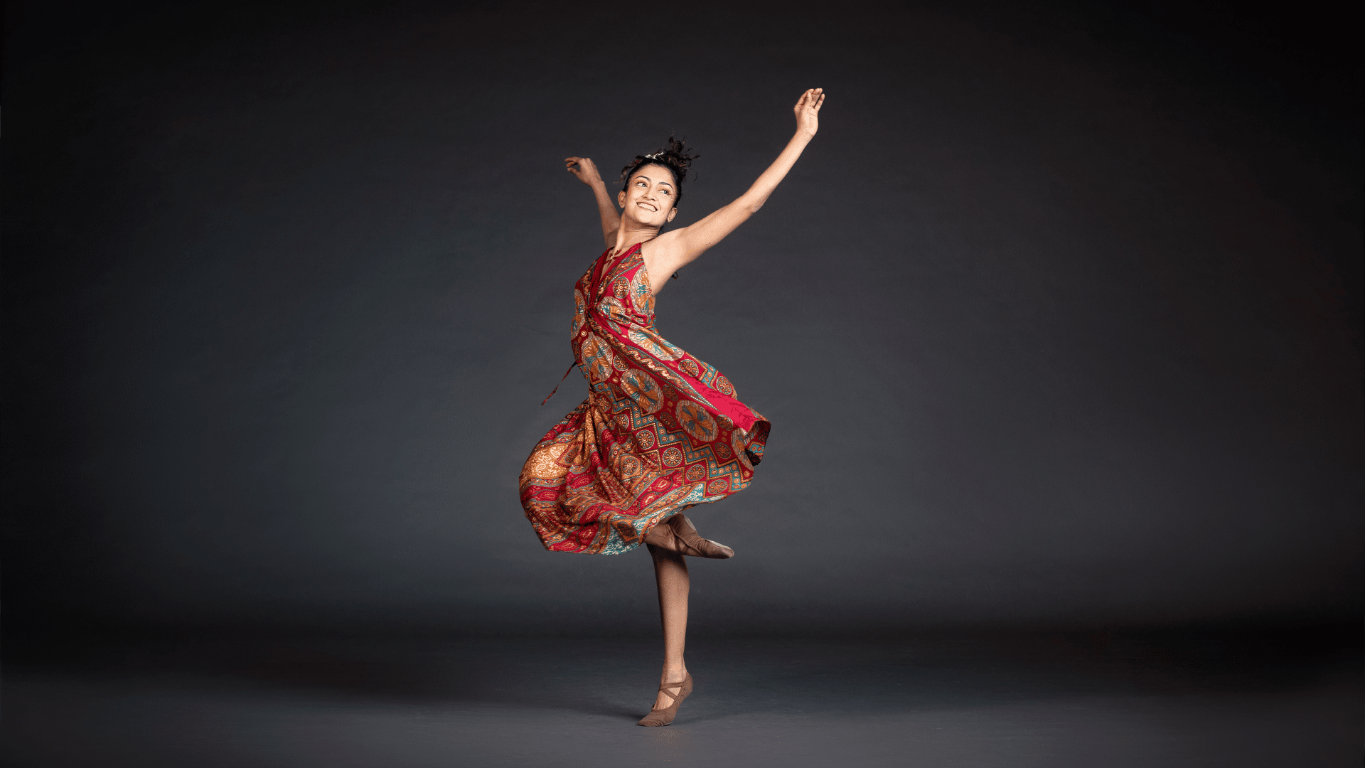 A ballet dancer balanced on one foot, arms outstretched, and smiling