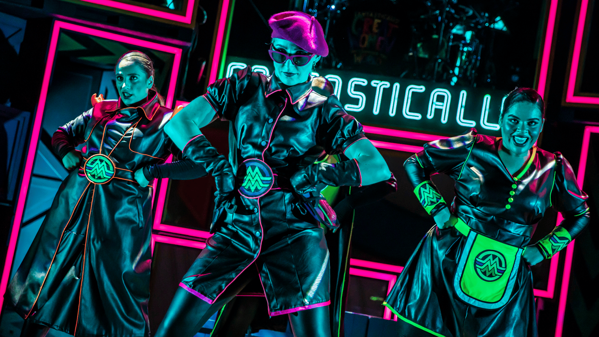 Three performers under neon lighting striking a pose