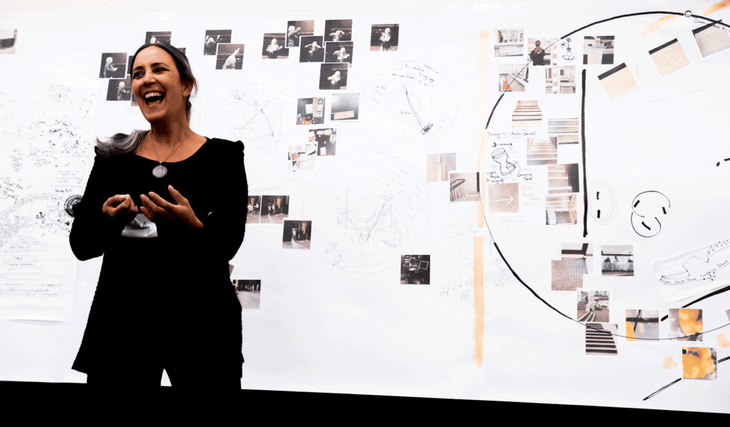 A woman laughs while standing in front of a whiteboard covered with drawings and printed photos