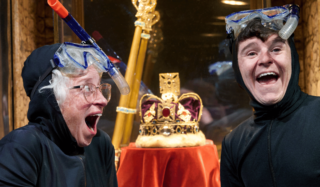 A young man and an older woman share a laugh in front of a golden crown and sceptre in a box