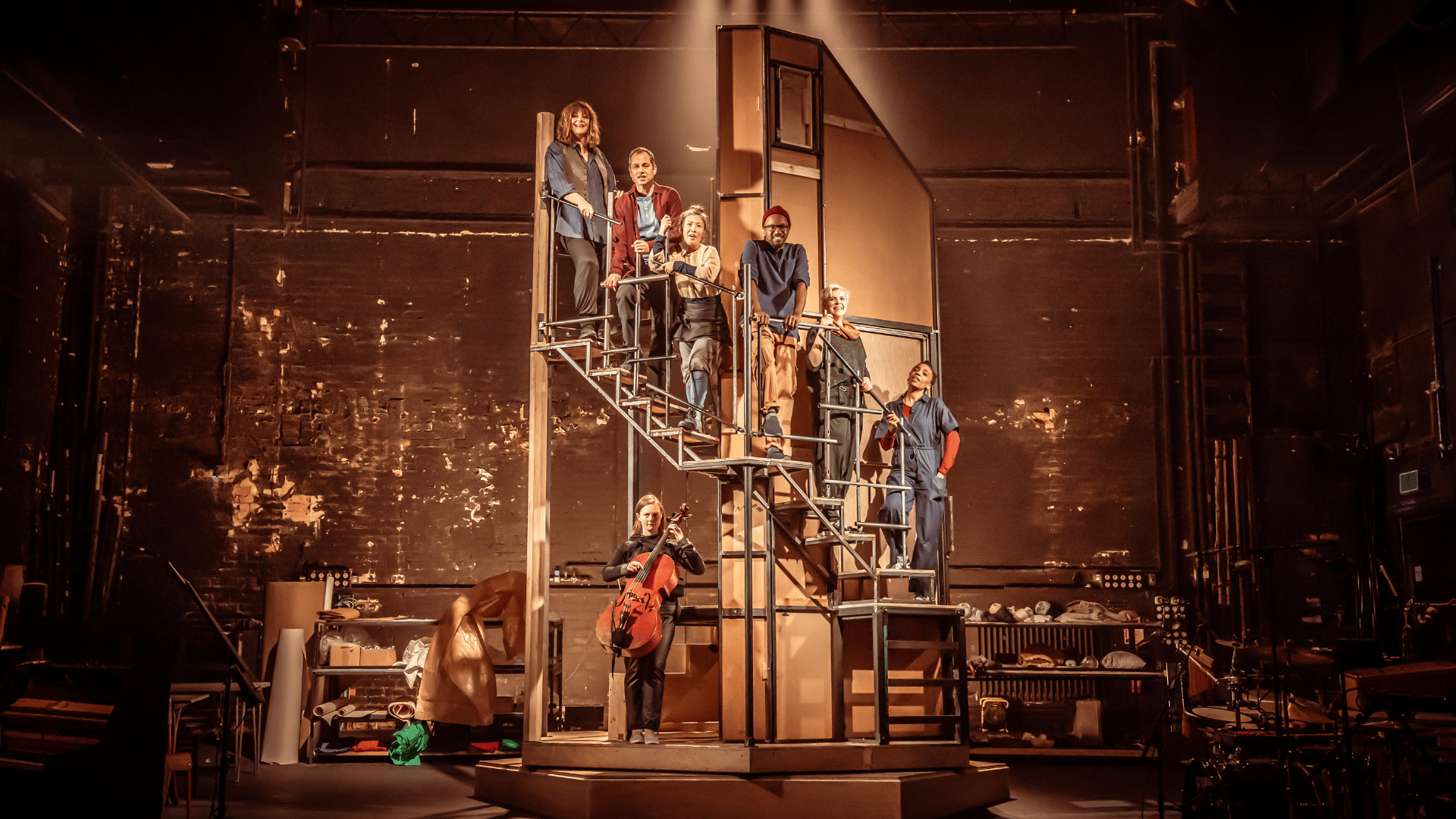 Improbable Musical cast in the middle of the stage, standing on a tall winding staircase